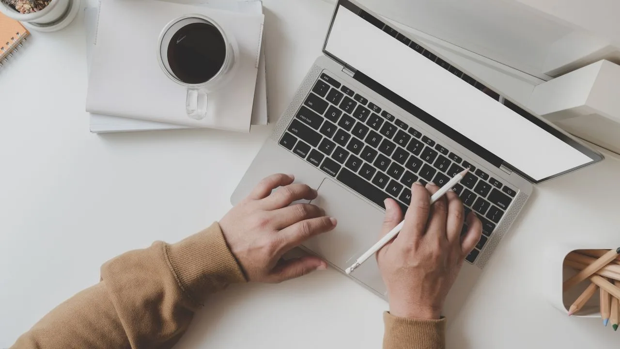 Closeup of person using a laptop with a cup of coffee and notebooks on the side. | Canadian tax deadline, tax filing.